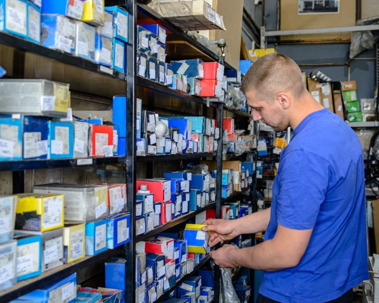 A Professional Car Maintenance Worker is Looking at how to Fix Car Problems on a Car and Looking for Aproppiate Part in the Storage.
